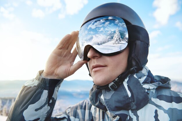 Portrait d'homme sur fond de ciel bleu détient des lunettes de ski avec le reflet des montagnes enneigées.. Sports d'hiver.