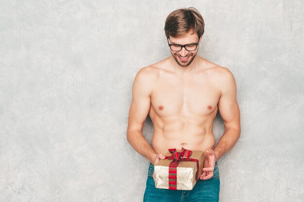 Portrait d'un homme fort beau sportif. Modèle de remise en forme athlétique sain posant près d'un mur gris en jeans.