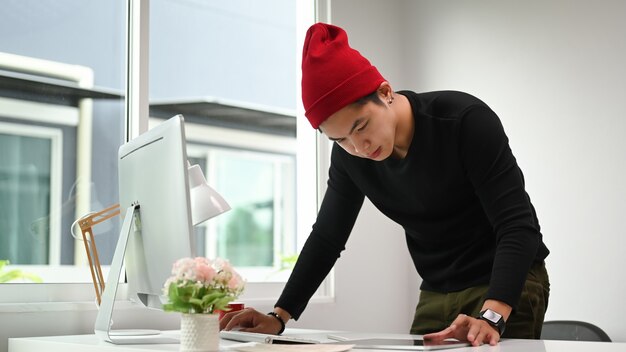 Portrait d'un homme graphiste en chapeau de laine rouge travaillant au bureau de création
