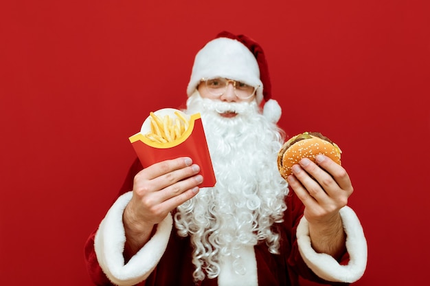 Portrait homme habillé en père Noël tenant un hamburger et des frites