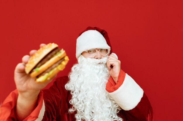 Portrait homme habillé en Père Noël tenant un hamburger