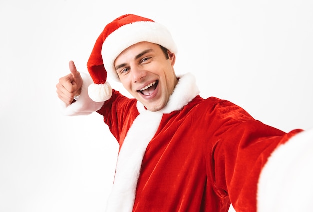 Portrait d'homme heureux des années 30 en costume de père Noël et chapeau rouge en riant tout en prenant selfie photo