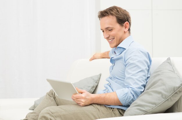 Portrait d'homme heureux sur canapé à la recherche de l'ordinateur portable