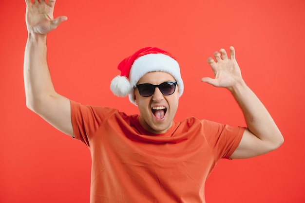 Portrait d'un homme heureux et excité en bonnet de noel se réjouissant et gagnant quelque chose célébrant le nouvel an debout sur fond rouge