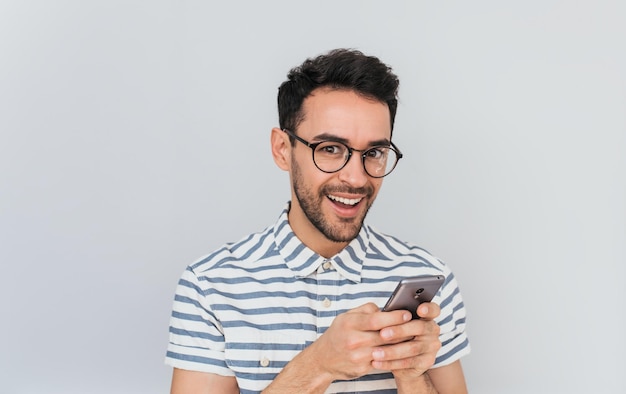 Portrait d'un homme heureux et surpris portant une chemise rayée et des lunettes de soleil à l'aide d'un téléphone intelligent pour envoyer des SMS ayant un sourire agréable montrant des dents blanches avait un visage étonné pour de bonnes nouvelles
