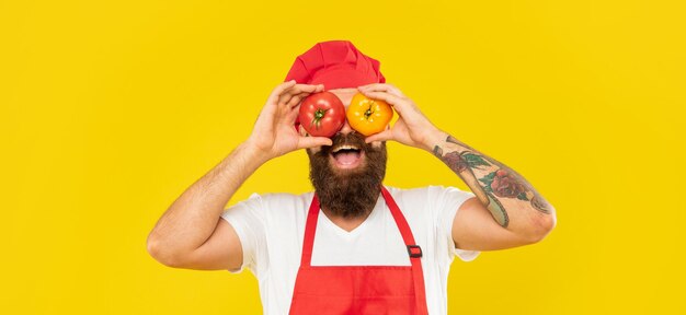 Portrait d'un homme heureux en tablier de cuisine et toque tenant des tomates sur les yeux fond jaune cuisinier