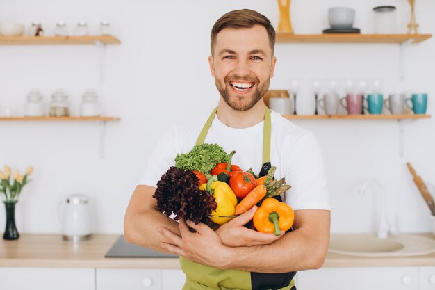 Portrait d'un homme heureux tenant une assiette de légumes frais dans la cuisine