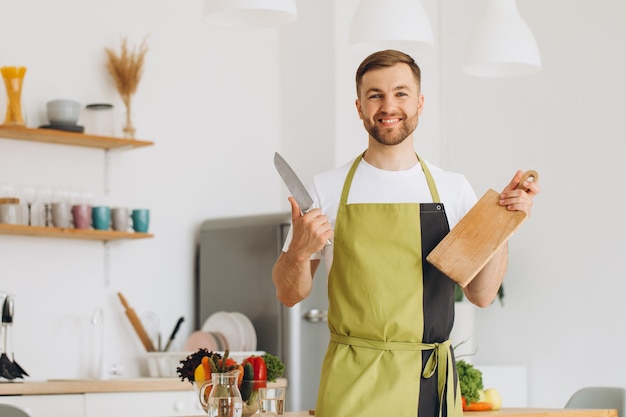 Portrait d'un homme heureux tenant une planche de cuisine et un couteau dans la cuisine à la maison