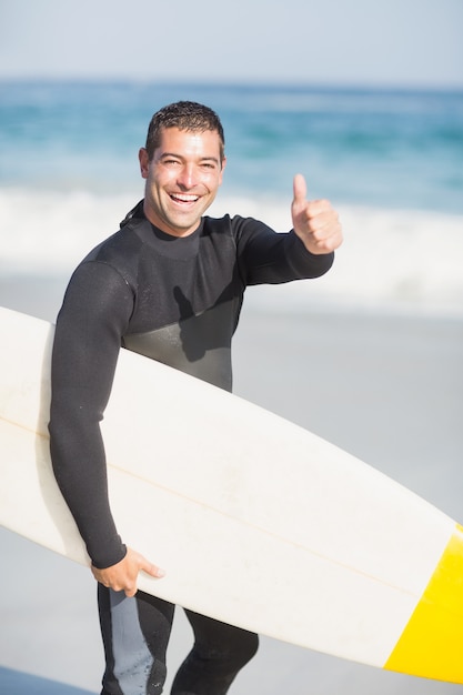 Portrait d'un homme heureux, tenant une planche de surf sur la plage