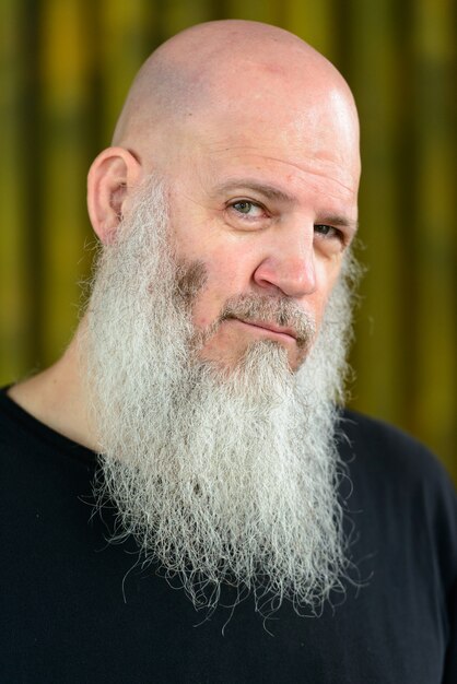 Portrait d'homme hipster chauve mature avec une longue barbe contre le mur de bambou à l'extérieur