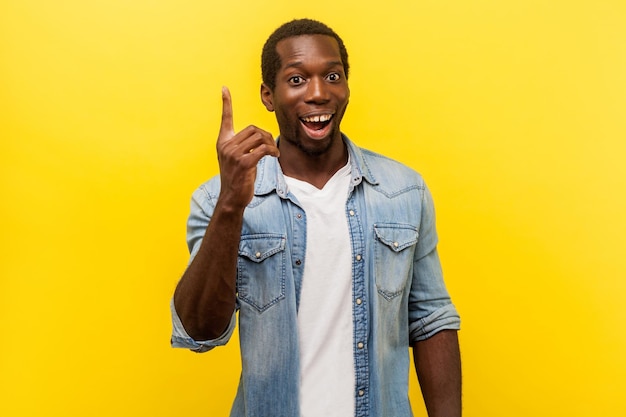 Portrait d'un homme inspiré créatif en chemise décontractée en denim pointant le doigt vers le haut montrant un signe d'idée formidable semblant surpris par une solution soudaine pensée de génie prise de vue en studio isolée sur fond jaune