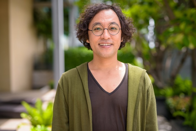 Portrait d'un homme japonais aux cheveux bouclés portant des lunettes avec la nature dans le jardin sur le toit à l'extérieur