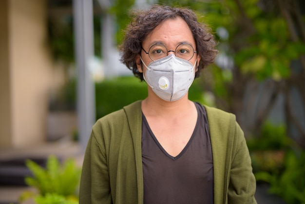 Portrait d'un homme japonais aux cheveux bouclés portant un masque de protection contre l'épidémie de virus corona dans le jardin sur le toit