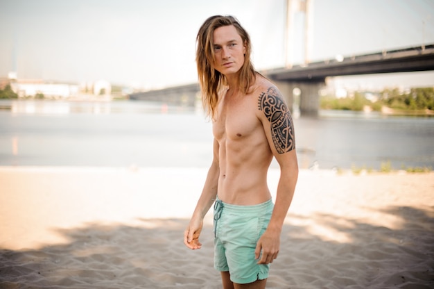 Portrait d'un homme jeune et mince aux cheveux longs sur la plage