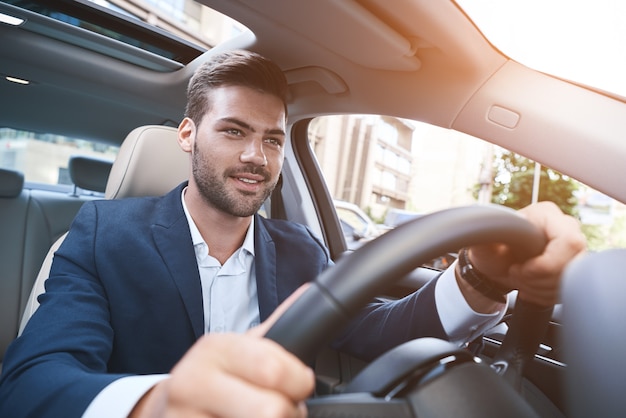 Portrait d'un homme joyeux conduisant une voiture en tenue de soirée et gardant han