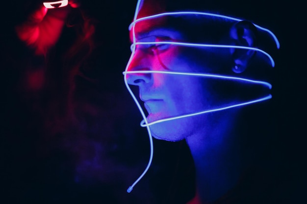 Portrait d'un homme avec des lignes de tubes lumineux au néon sur son visage dans l'obscurité Concept cyberpunk et réalité virtuelle