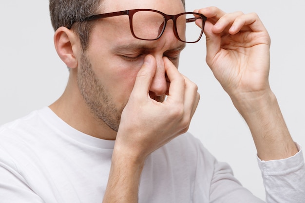 Portrait d'homme à lunettes se frottant les yeux et le nez, se sent fatigué après avoir travaillé sur un ordinateur portable, isolé