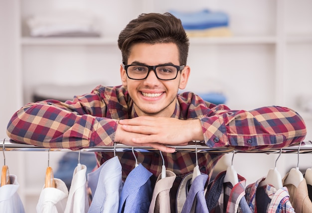 Portrait d'un homme à lunettes se penchant sur un rack avec des vêtements.