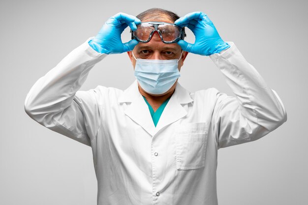 Portrait d'homme médecin senior en masque décollant des lunettes de protection