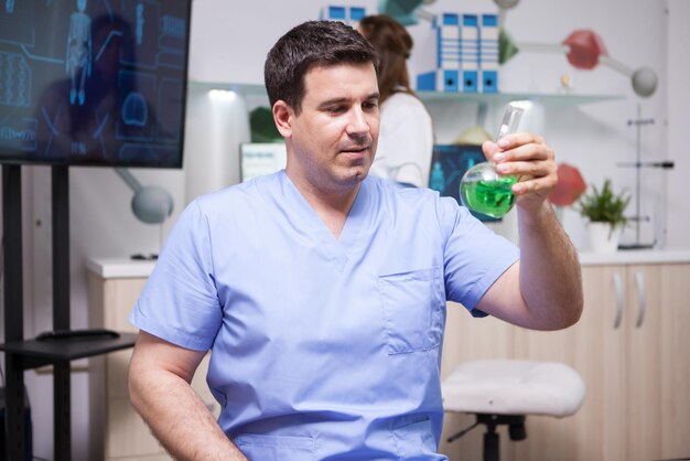 Portrait d'un homme microbiologiste tenant un tube à essai avec une solution verte en laboratoire scientifique. Test génétique.