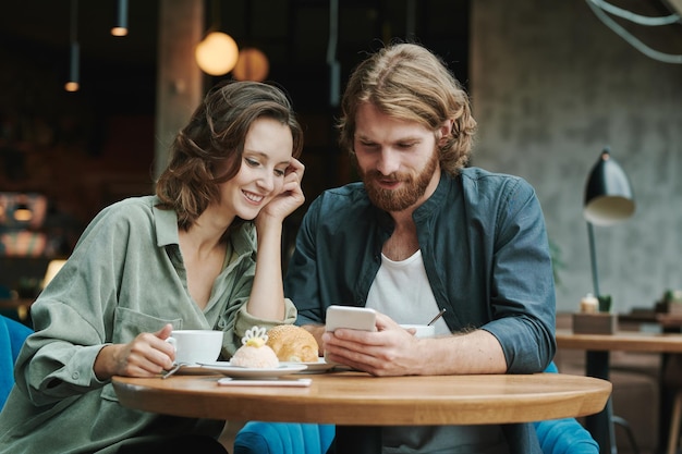 Portrait d'un homme moderne sérieux avec barbe assis à une table ronde dans un café loft et appelant par mobile