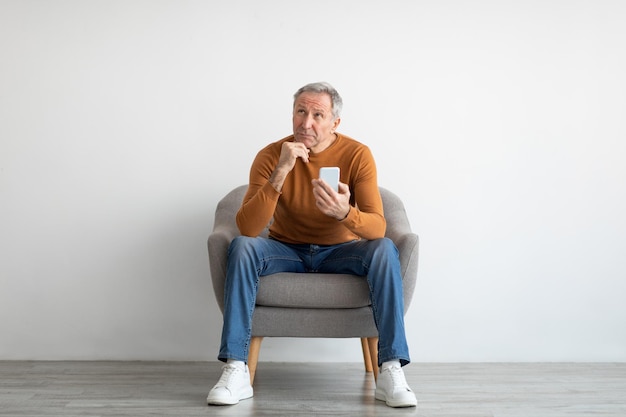 Portrait d'homme mûr à l'aide de smartphone assis sur un fauteuil