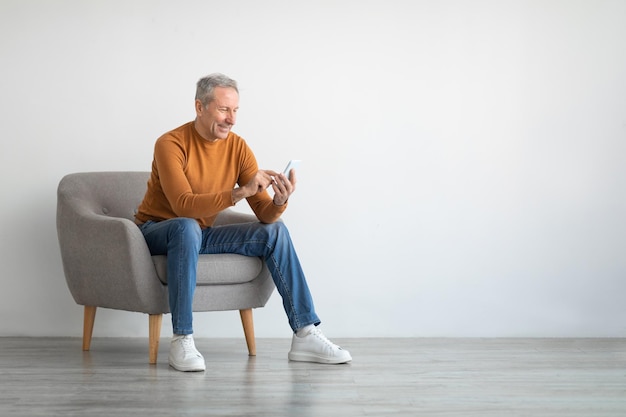 Portrait d'homme mûr à l'aide de smartphone assis sur un fauteuil