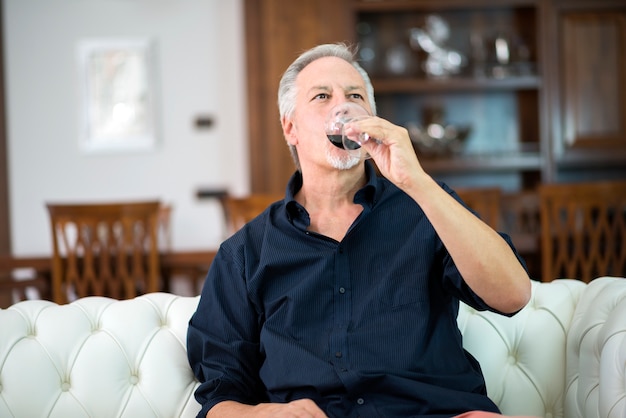 Portrait d&#39;un homme mûr en dégustant un verre de vin rouge à la maison