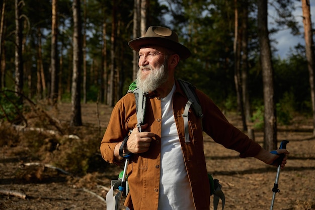 Portrait d'un homme mûr et souriant, touriste avec des bâtons scandinaves, passant une journée à l'extérieur et profitant d'une activité de randonnée
