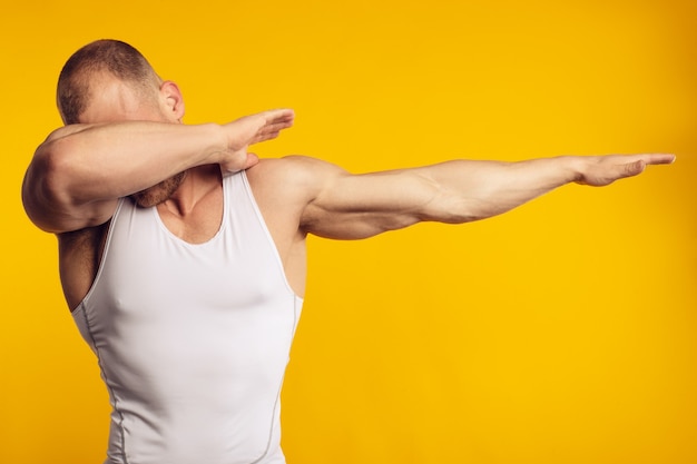 Portrait d'homme musclé en chemise blanche, faisant dab debout sur un mur jaune isolé