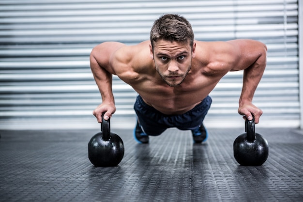 Portrait d&#39;un homme musclé faisant des pompes avec des kettlebells