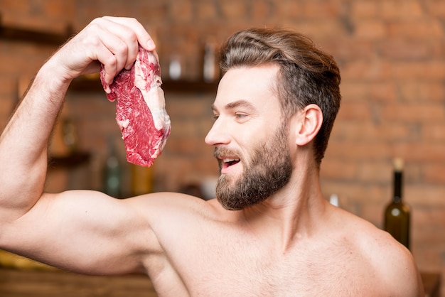 Portrait d'un homme musclé nu avec de la viande crue dans la cuisine