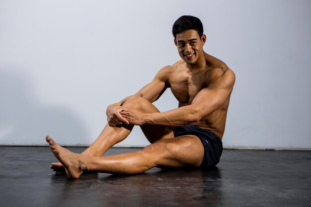 Photo portrait d'un homme musclé sans chemise assis contre le mur