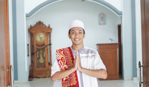 Un portrait d'un homme musulman asiatique se lève dans une pose de bienvenue aux mains de Namaste, accueillant les invités, Ied Fitr salutation à la mosquée