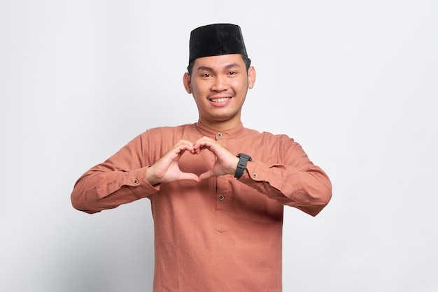 Portrait d'un homme musulman asiatique souriant montrant un geste cardiaque et regardant la caméra isolée sur fond blanc