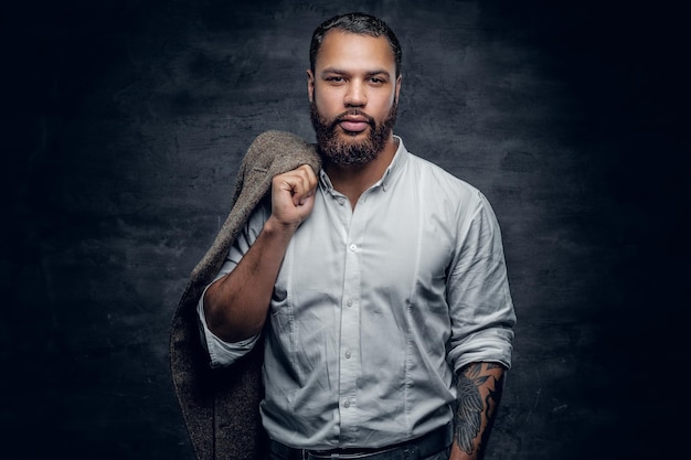 Portrait d'homme noir barbu avec bras tatoué portant une chemise blanche.