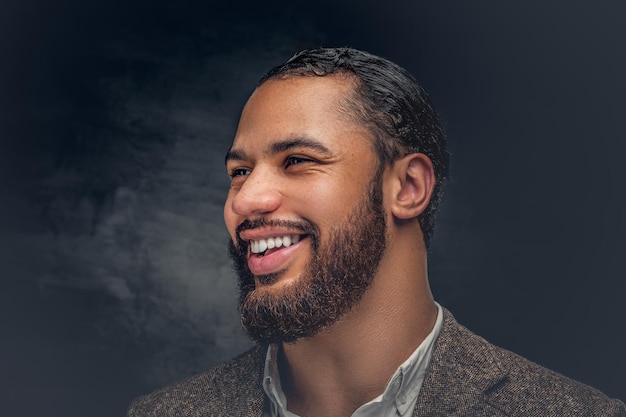 Portrait d'un homme noir souriant sur fond gris foncé.