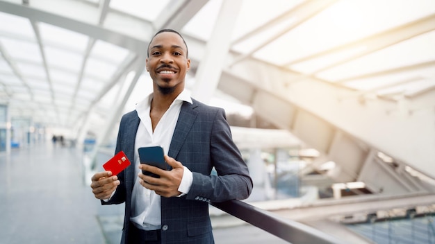 Portrait d'un homme noir souriant avec smartphone et carte de crédit à l'aéroport