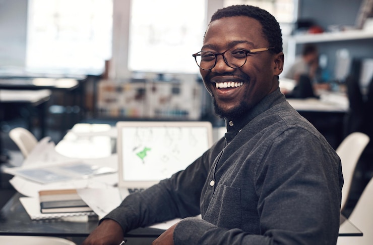 Photo portrait d'homme noir sourire et ordinateur portable par bureau pour les entreprises de construction en démarrage et la recherche dans le bureau architecte africain entrepreneur et ordinateur pour le logiciel de rendu de courrier électronique et la conception de propriété