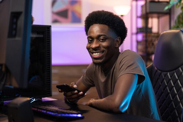 Portrait d'un homme à la peau sombre assis confortablement sur une chaise au bureau des joueurs garçon tient le téléphone