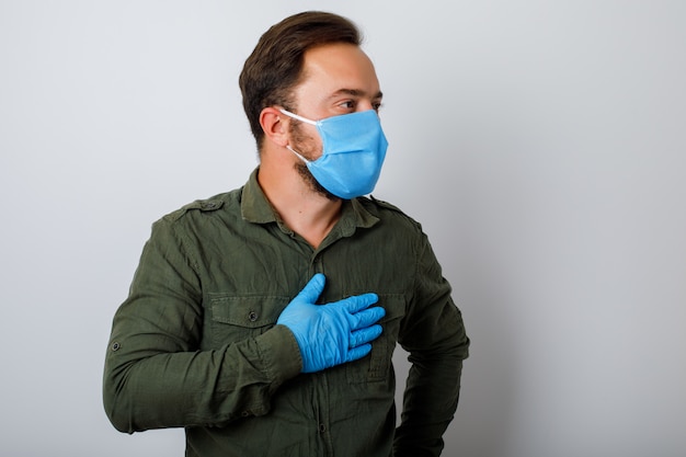 Portrait homme portant un masque facial avec toux et fièvre, isolé sur mur blanc. Soins de santé et concept médical.