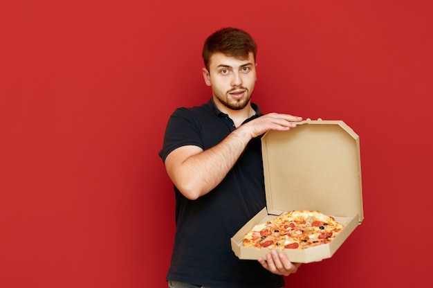 Portrait d'homme positif se dresse et ouvre la boîte de délicieuses pizzas fraîches