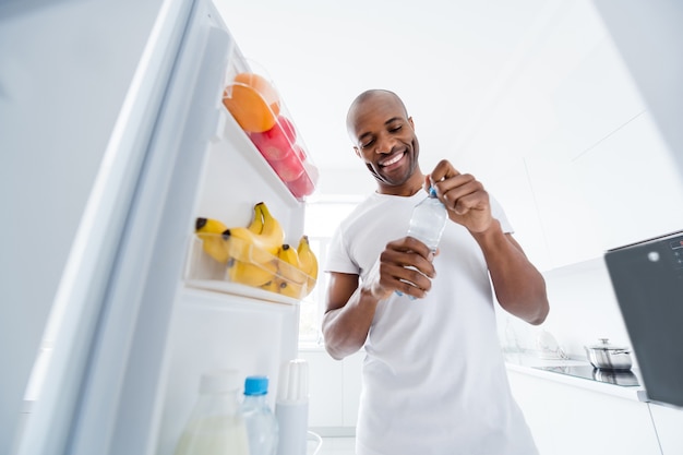 Portrait d'un homme regardant dans un réfrigérateur prenant des collations dans le régime de vie des soins de santé dans la cuisine à l'intérieur