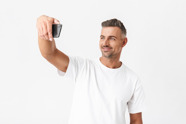 Portrait d'un homme réussi des années 30 portant un t-shirt décontracté prenant un selfie isolé sur blanc