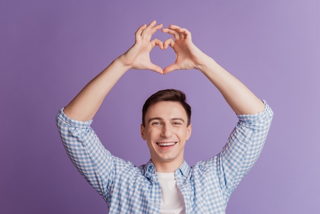 Portrait d'un homme romantique rêveur montrant le symbole du coeur d'amour sur fond violet