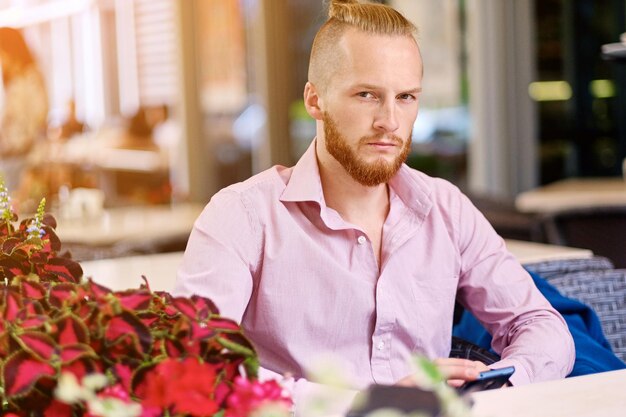 Portrait d'homme rousse barbu dans un shirtt rose à la table dans un café.