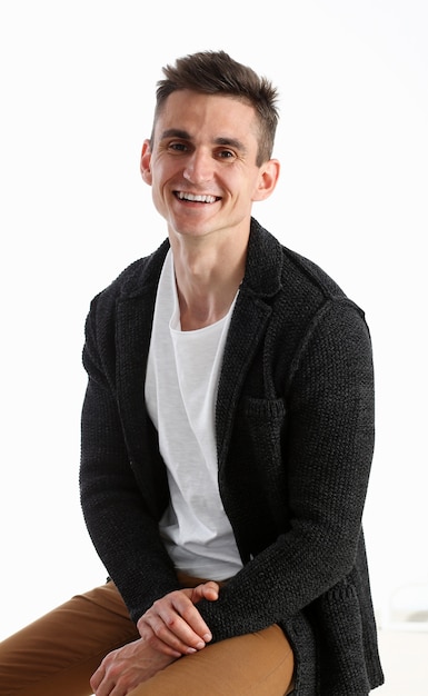 Portrait d'un homme séduisant dans un pull et un T-shirt, assis sur une chaise et souriant