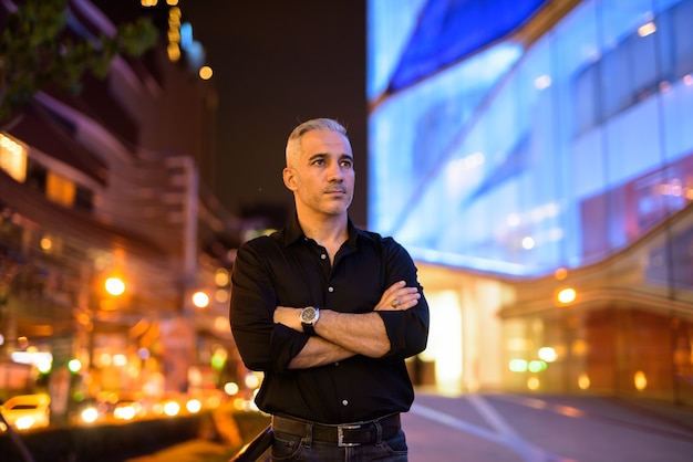 Portrait d'homme séduisant pensant la nuit dans les rues les bras croisés