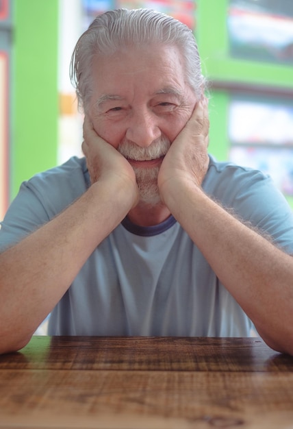 Portrait d'un homme senior caucasien assis à une table de café avec les mains sur son visage