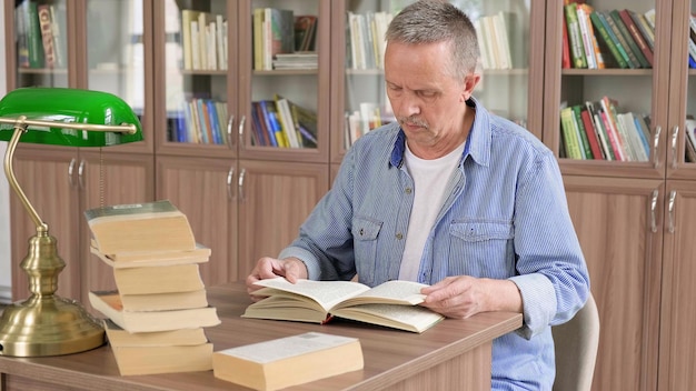 Portrait d'un homme senior caucasien travaillant avec un livre dans une bibliothèque publique Étudiant adulte à la bibliothèque